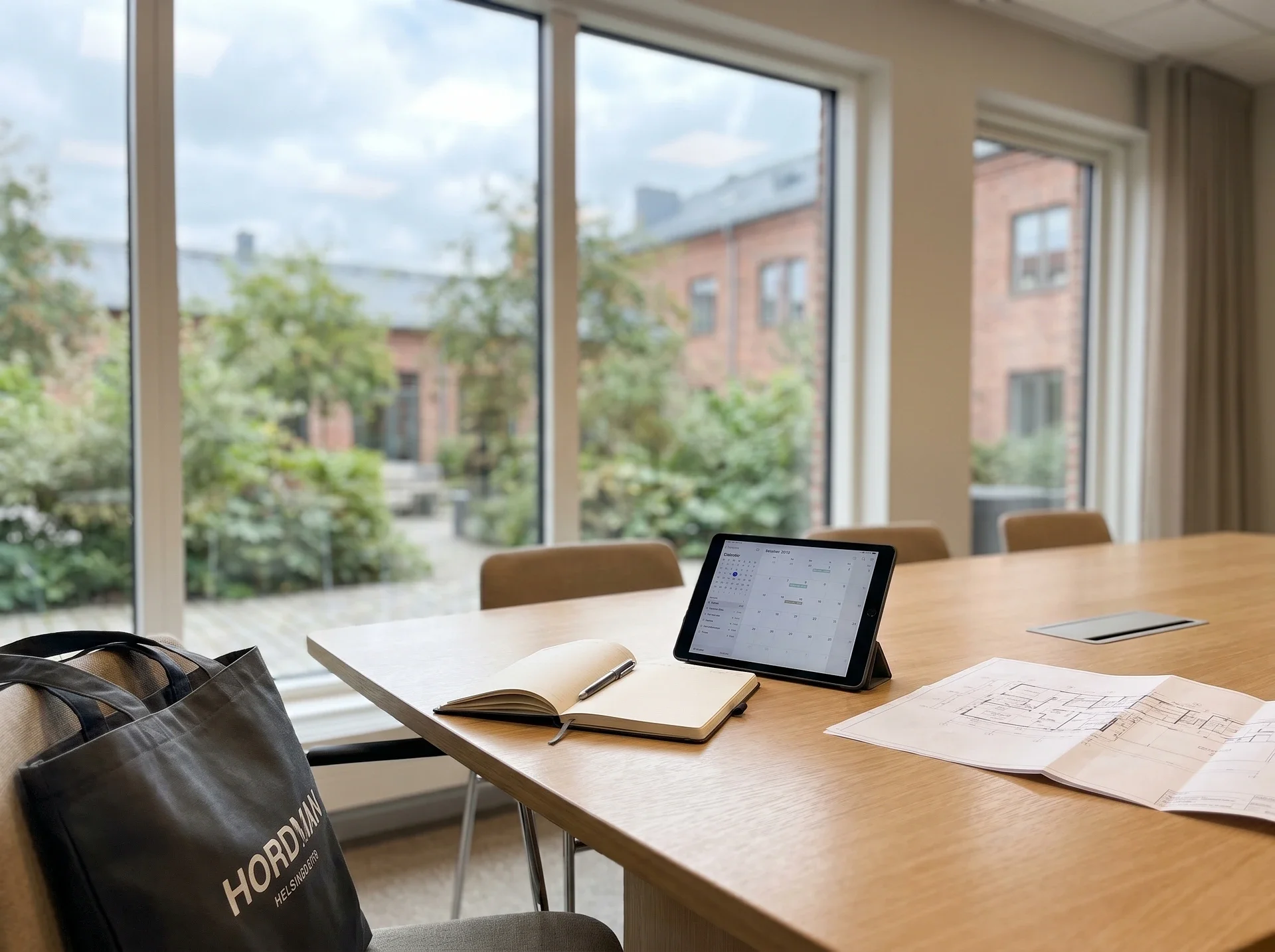 Konferensrum med iPad, anteckningsblock och ritningar på träbord.