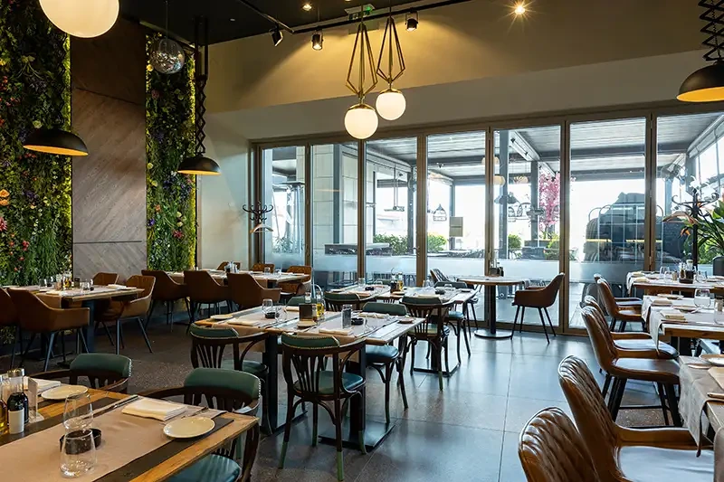 Elegant restauranginteriör med gröna väggar, moderna lampor och bruna stolar.
