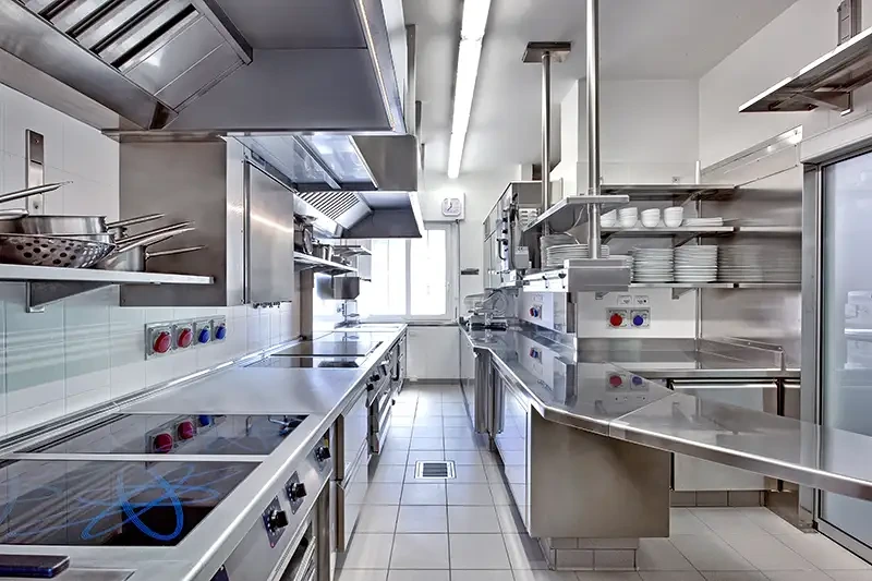 Modernt rostfritt professionellt storkök med ugnar, hyllor och ventilation.